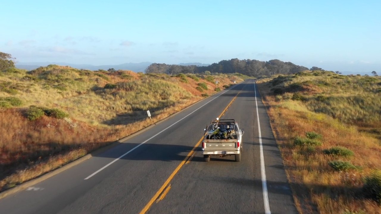 A pickup truck driving down an open road, seen from a drone