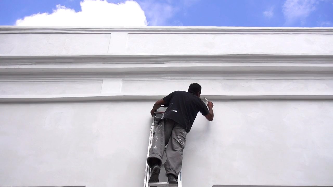 A painter on a ladder painting a building facade